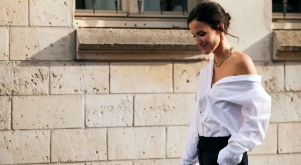Donna con camicia bianca oversize e pantaloni neri, un look smart casual con una collana dorata.