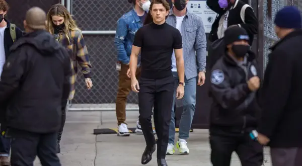 Tom Holland indossa un outfit elegante con scarpe perfette per pantaloni a sigaretta donna, mentre cammina con un gruppo di persone.
