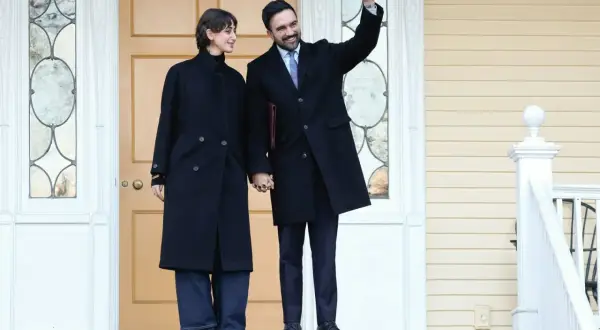 Una coppia, lui saluta, si tiene per mano davanti a una porta. Un'atmosfera da rama duwaji.