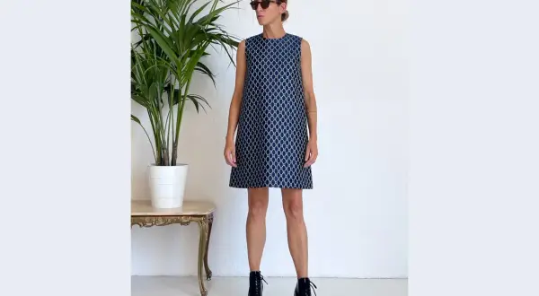 Donna con occhiali da sole indossa un vestito a trapezio blu con fantasia geometrica bianca. Un look moderno che sta bene a molte fisicità.