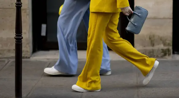 Un outfit tailleur con sneakers, giallo vivace e azzurro pastello, camminano sul marciapiede.