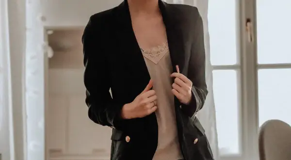Donna con tailleur nero, indossa una camicetta di pizzo color crema sotto. Un'idea su cosa mettere sotto un tailleur nero.