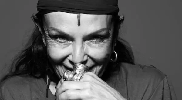 Michele Lamy, con un turbante nero e un segno sulla fronte, sorride enigmaticamente, le mani adornate da anelli vistosi.
