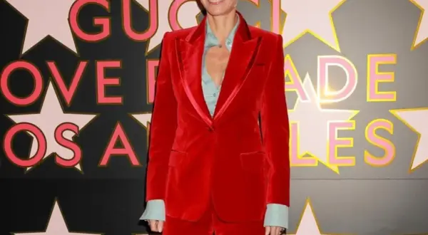 Gwyneth Paltrow in un completo rosso di velluto, sorride davanti a uno sfondo con stelle e lettere rosa e oro.