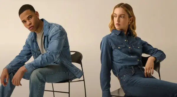 Coppia in total look denim. Lui con giacca e jeans, lei con camicia e jeans, entrambi con un fit che si stringe verso il basso, il tapered fit significato.