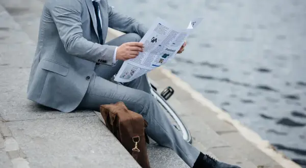Uomo in vestito grigio legge il giornale, con scarpe nere eleganti. Un dilemma: vestito grigio che scarpe abbinare?