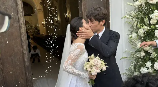 Alessandra Mastronardi e il suo sposo si baciano fuori dalla chiesa, tra petali di fiori e un'atmosfera di gioia per il loro matrimonio.