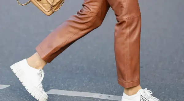 Un outfit chic con pantaloni in pelle marrone e sneakers bianche donna Prada. Una borsa Chanel completa il look.