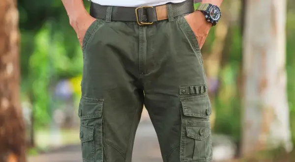 Uomo con outfit composto da pantaloni cargo verdi, cintura in tessuto e orologio sportivo.