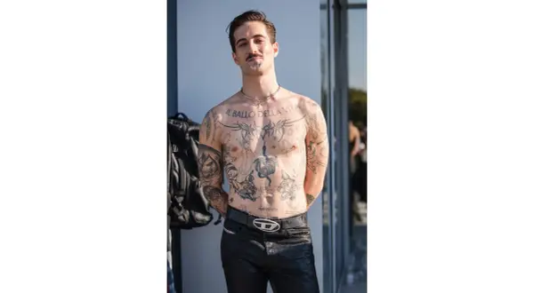 Damiano David, a torso covered in tattoos, poses confidently.