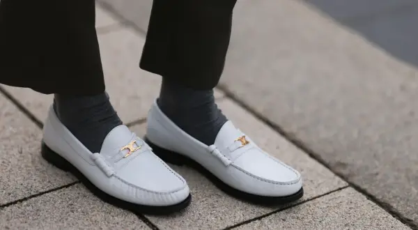Scarpe pulite bianche con fibbia dorata, calzini grigi e pantaloni scuri.