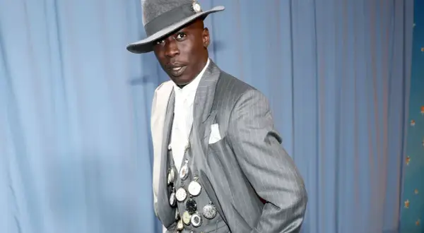 Un uomo con un cappello grigio e un completo gessato, ornato da numerosi orologi da taschino, incarna l'eleganza maschile.