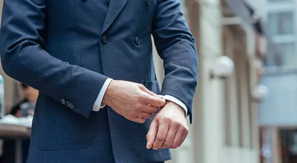 Uomo che sistema il polsino della sua giacca blu, un perfetto abbinamento giacca blu uomo per un look elegante.