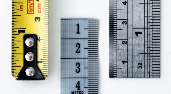 Tre metri diversi mostrano come si misura il tacco di una scarpa: uno giallo con indicazioni in pollici e centimetri, uno azzurro con numeri grandi e uno metallico con tacche precise.