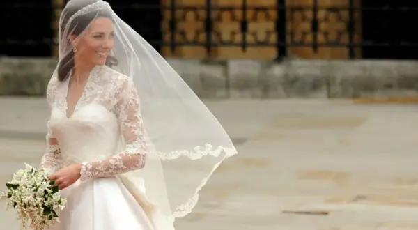 Kate Middleton sposa, radiosa nel suo abito bianco con pizzo e velo, tiene un bouquet di fiori.