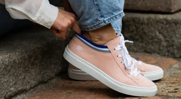 Mani che sistemano calzini a righe dentro scarpe rosa cipria, un dettaglio per il riempimento scarpe grandi.