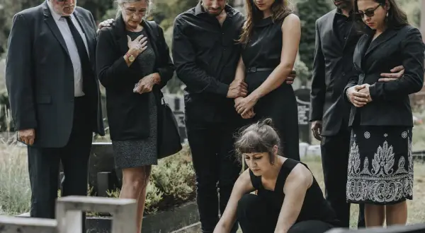 Famiglia in lutto, vestiti di nero per un funerale. Una donna depone fiori sulla tomba.