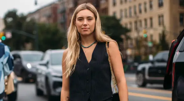 Donna con capelli biondi indossa un elegante gilet doppiopetto a righe, collana turchese e borsa a tracolla dorata, in strada.