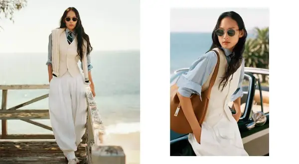 Donna in stile smart casual con pantaloni bianchi ampi, gilet e camicia azzurra, con un tocco di eleganza sulla passerella vista mare.
