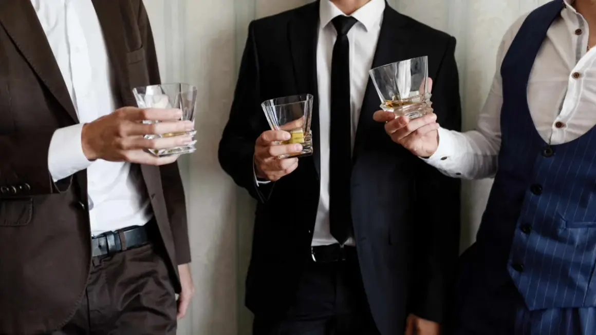 Uomini eleganti con bicchieri di whisky, perfetti per un dress code cocktail.
