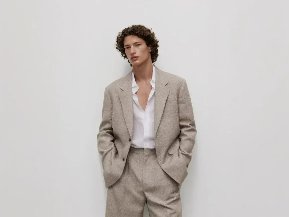 Uomo con giacca beige e camicia bianca sbottonata: un'idea di cosa mettere sotto la giacca uomo per un look casual-chic.