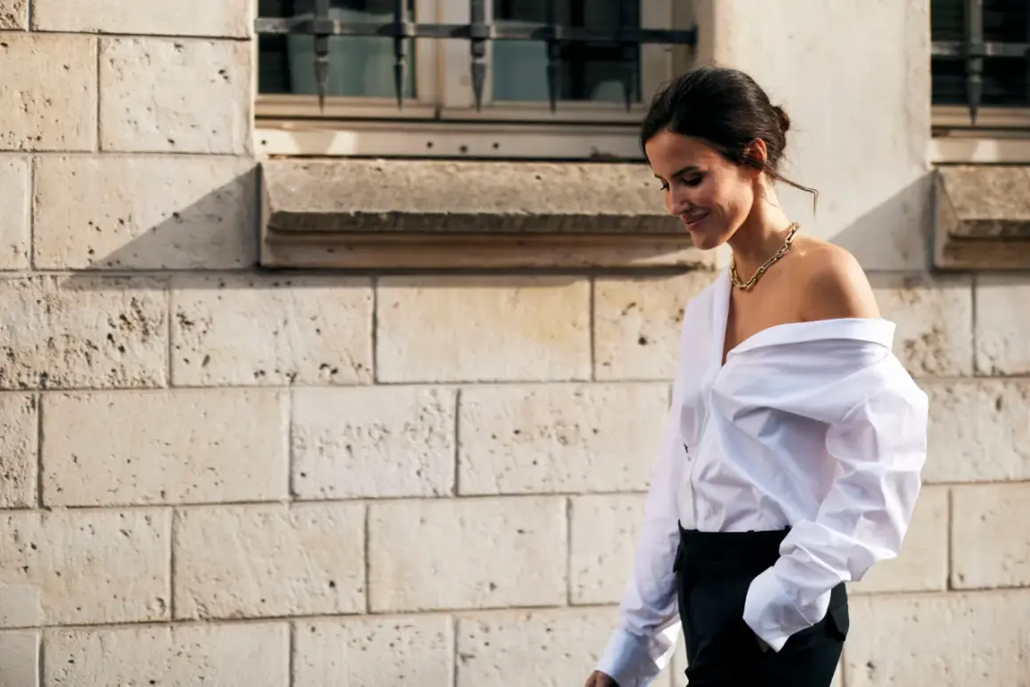 Donna con camicia bianca oversize e pantaloni neri, un look smart casual con una collana dorata.