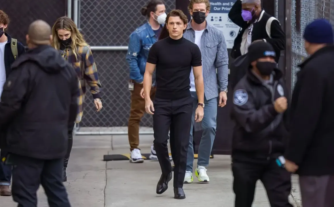 Tom Holland indossa un outfit elegante con scarpe perfette per pantaloni a sigaretta donna, mentre cammina con un gruppo di persone.