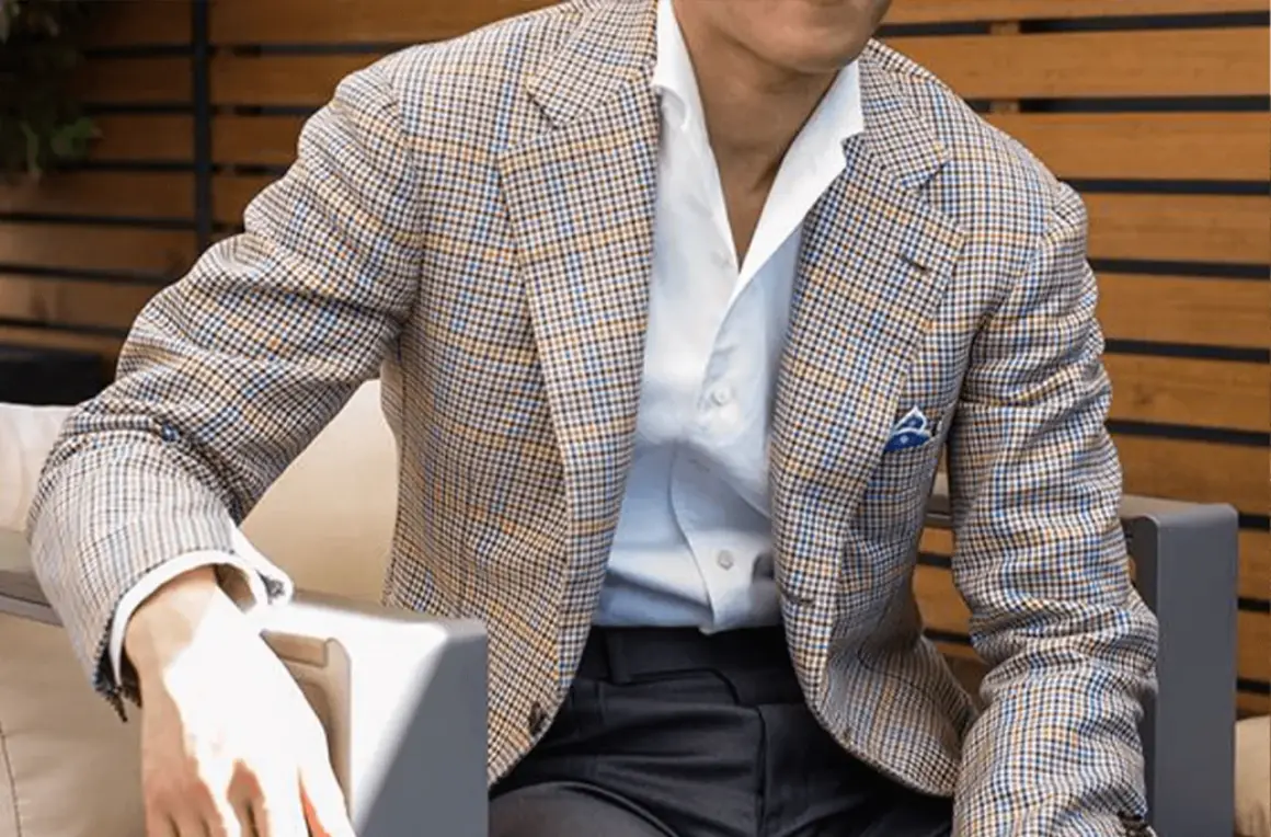 Uomo con giacca a quadri marrone, blu e arancione, camicia bianca e fazzoletto blu. Collezione drop 4.
