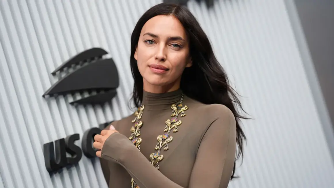 Irina Shayk, con un look audace e una collana d'oro, posa davanti a un logo.