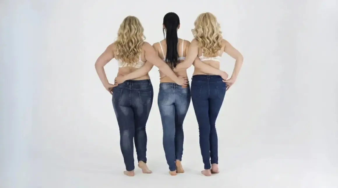 Tre donne in jeans e reggiseno, con le braccia incrociate sulla schiena. Un modo per far sembrare più alti.