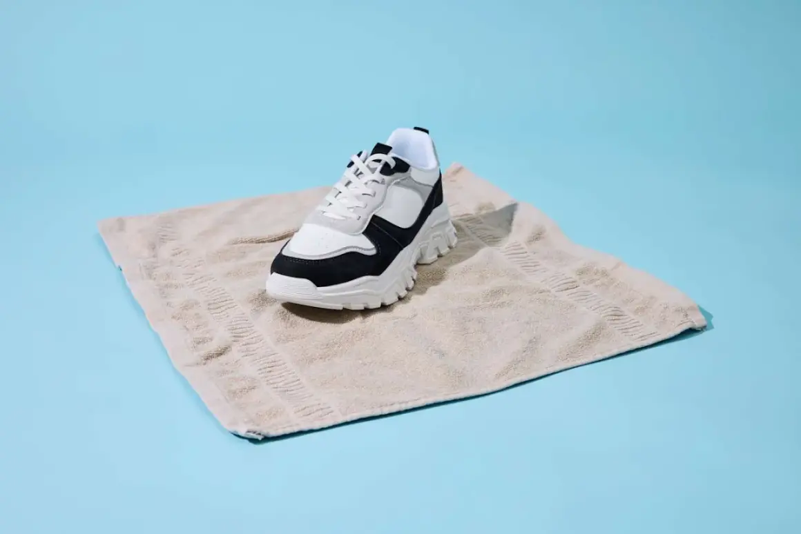 Sneaker bianco e nero su asciugamano beige, un metodo per asciugare scarpe bagnate dentro.
