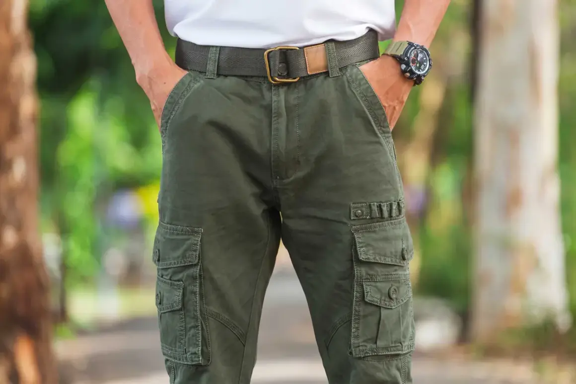 Uomo con outfit composto da pantaloni cargo verdi, cintura in tessuto e orologio sportivo.