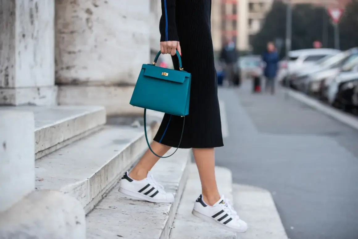 Scarpe da ginnastica bianche con strisce nere abbinate a un tubino nero e una borsa turchese.