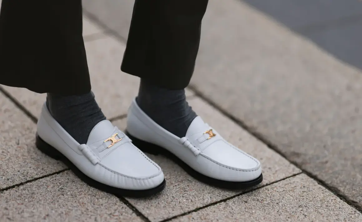 Scarpe pulite bianche con fibbia dorata, calzini grigi e pantaloni scuri.