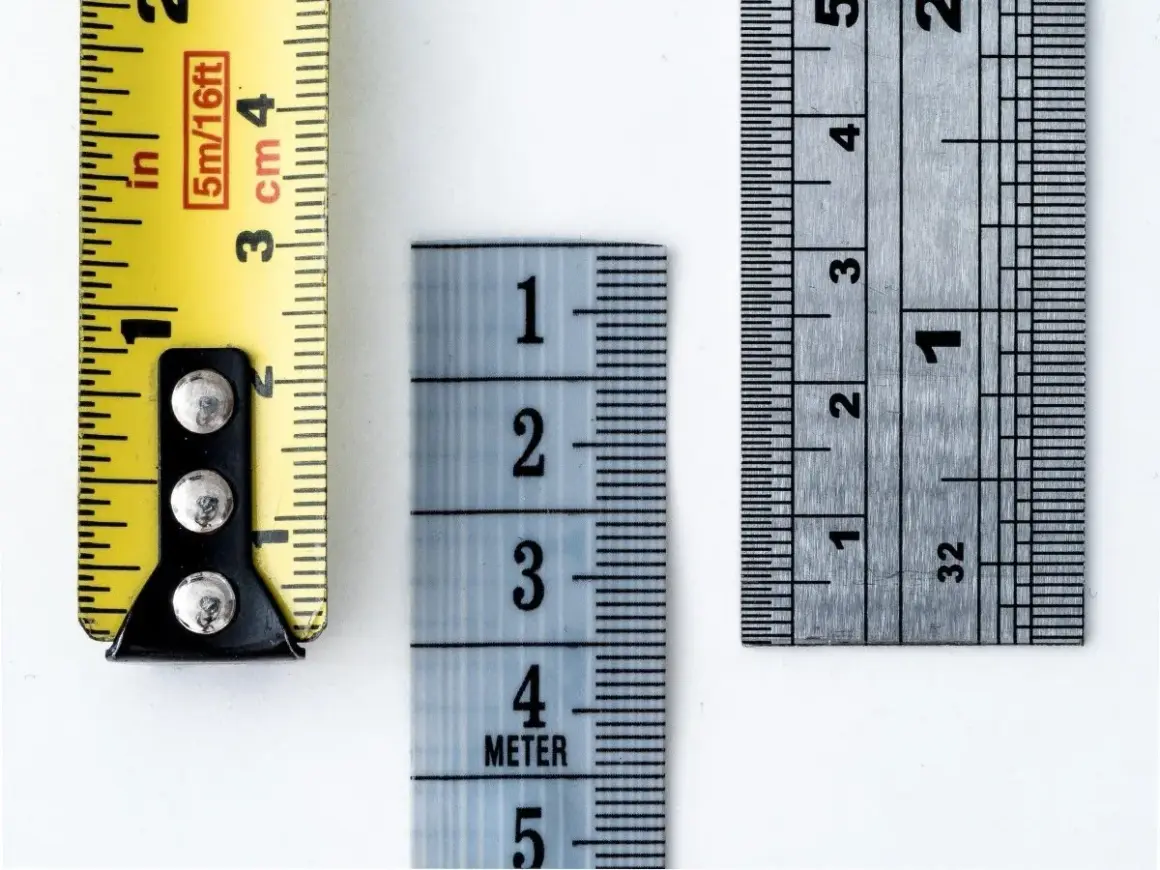 Tre metri diversi mostrano come si misura il tacco di una scarpa: uno giallo con indicazioni in pollici e centimetri, uno azzurro con numeri grandi e uno metallico con tacche precise.
