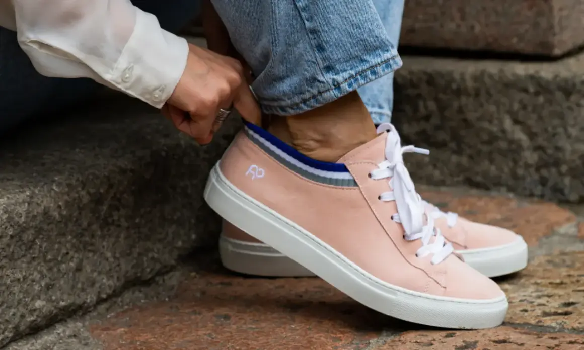 Mani che sistemano calzini a righe dentro scarpe rosa cipria, un dettaglio per il riempimento scarpe grandi.