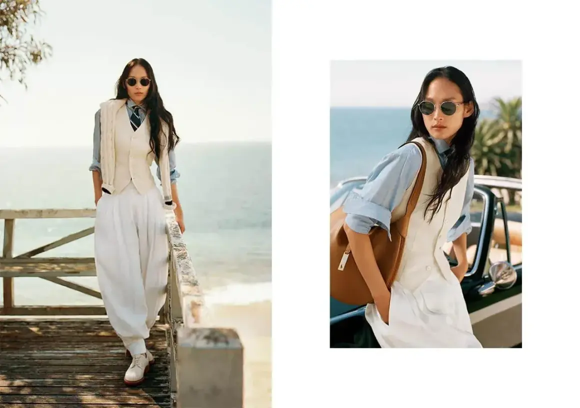 Donna in stile smart casual con pantaloni bianchi ampi, gilet e camicia azzurra, con un tocco di eleganza sulla passerella vista mare.