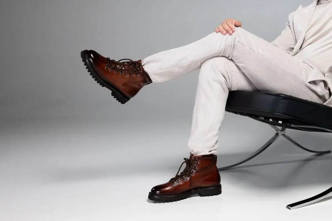 Un uomo indossa un outfit elegante con stivaletti marroni uomo, pantaloni chiari a coste e giacca coordinata, seduto su una poltrona moderna.