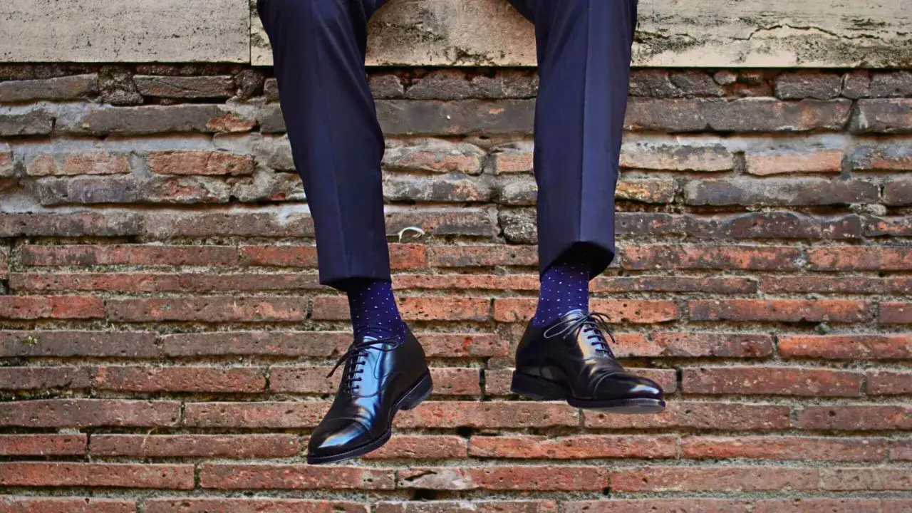 Un uomo indossa un abito blu scuro con calze blu a pois bianchi e scarpe nere lucide. L'abbinamento calze abito uomo è curato nei minimi dettagli.