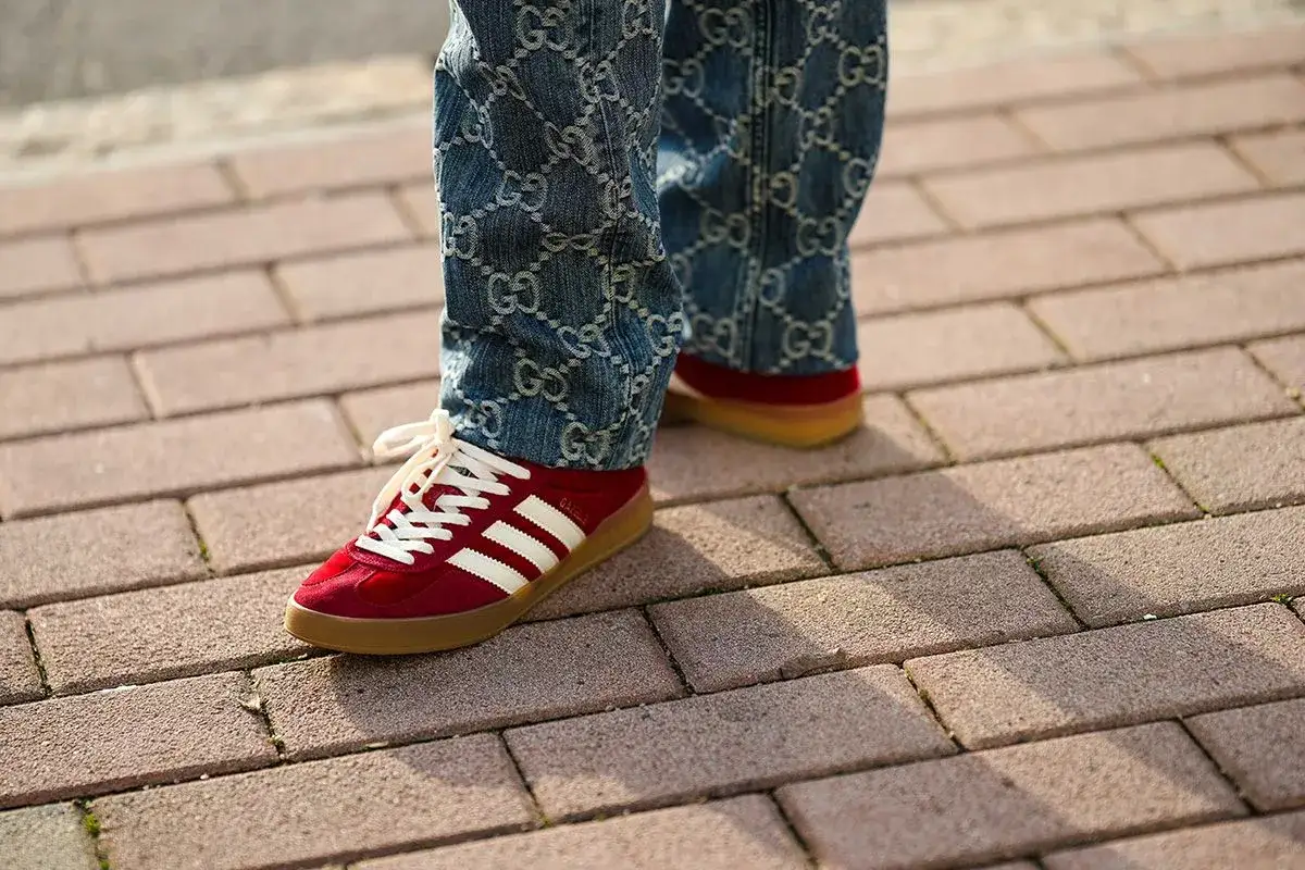 Un uomo con jeans Gucci e un paio di scarpe rosse Adidas Gazelle. Un look audace per chi ama abbinare scarpe rosse uomo con stile.