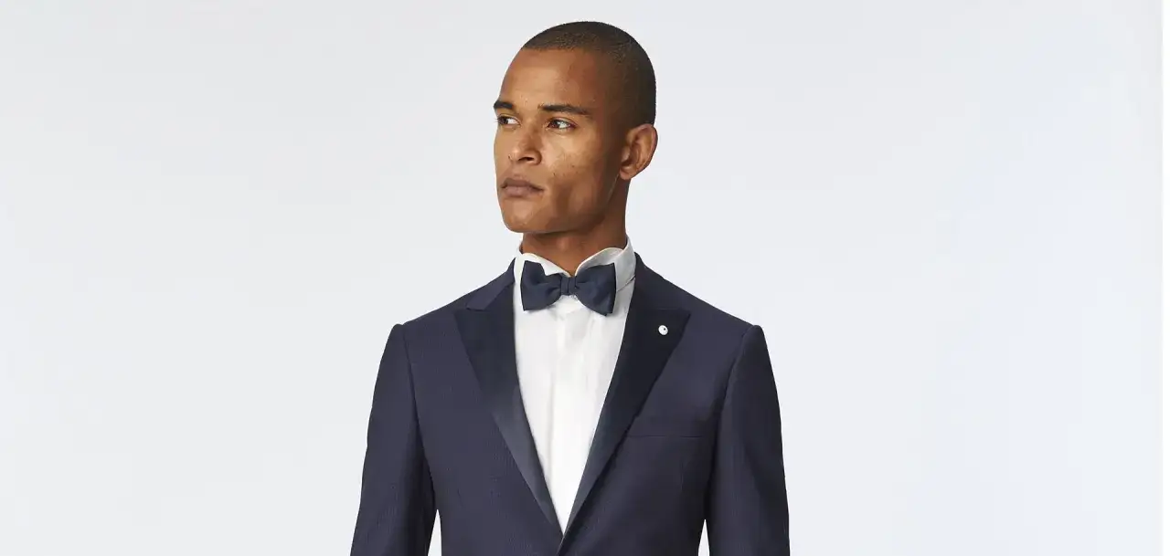 Uomo elegante in abito blu scuro con papillon blu navy, perfetto per un black tie dress code.