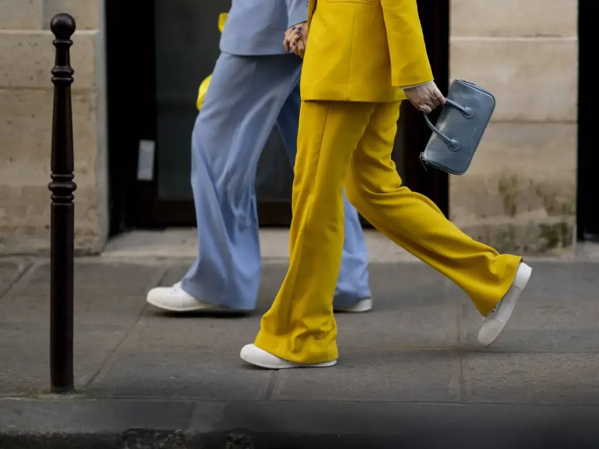 Un outfit tailleur con sneakers: pantaloni a zampa gialli e azzurri, abbinati a scarpe da ginnastica bianche.