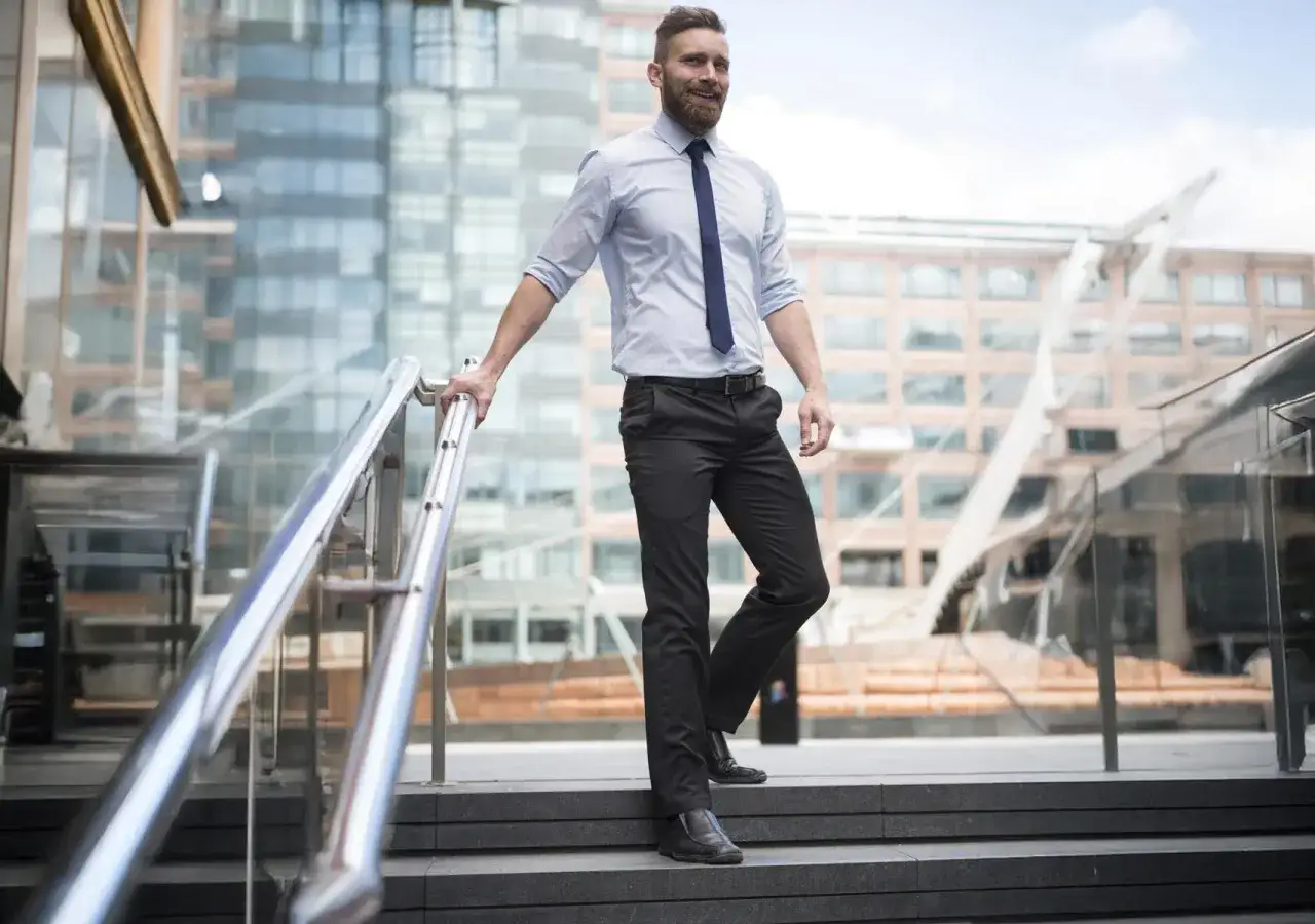 Uomo con pantaloni neri eleganti, camicia azzurra e cravatta blu, in un contesto urbano moderno. Perfetto per capire come abbinare pantaloni neri eleganti uomo.