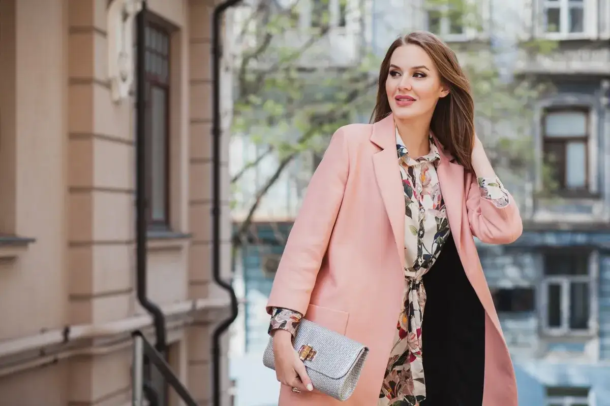 Donna elegante con blazer rosa, camicia floreale e pochette argentata, un'idea su come vestirsi a un battesimo con stile.