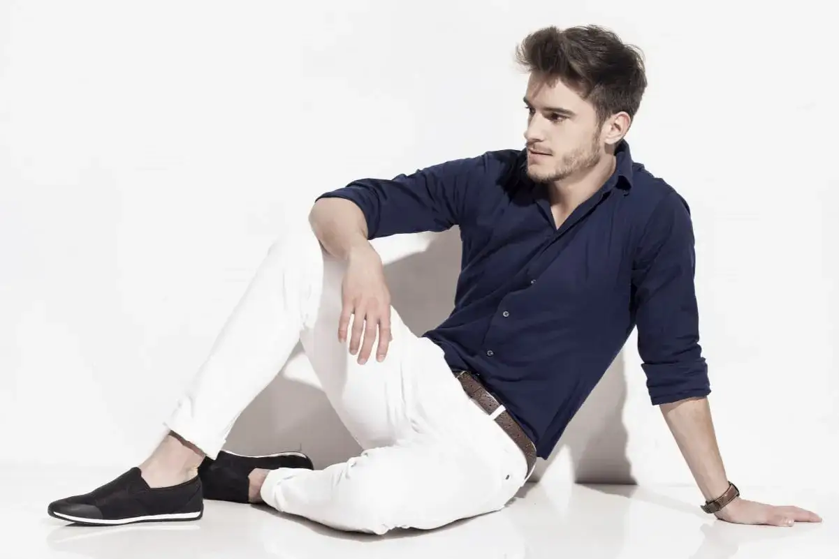 Uomo con camicia blu e pantaloni bianchi, indossa scarpe nere.