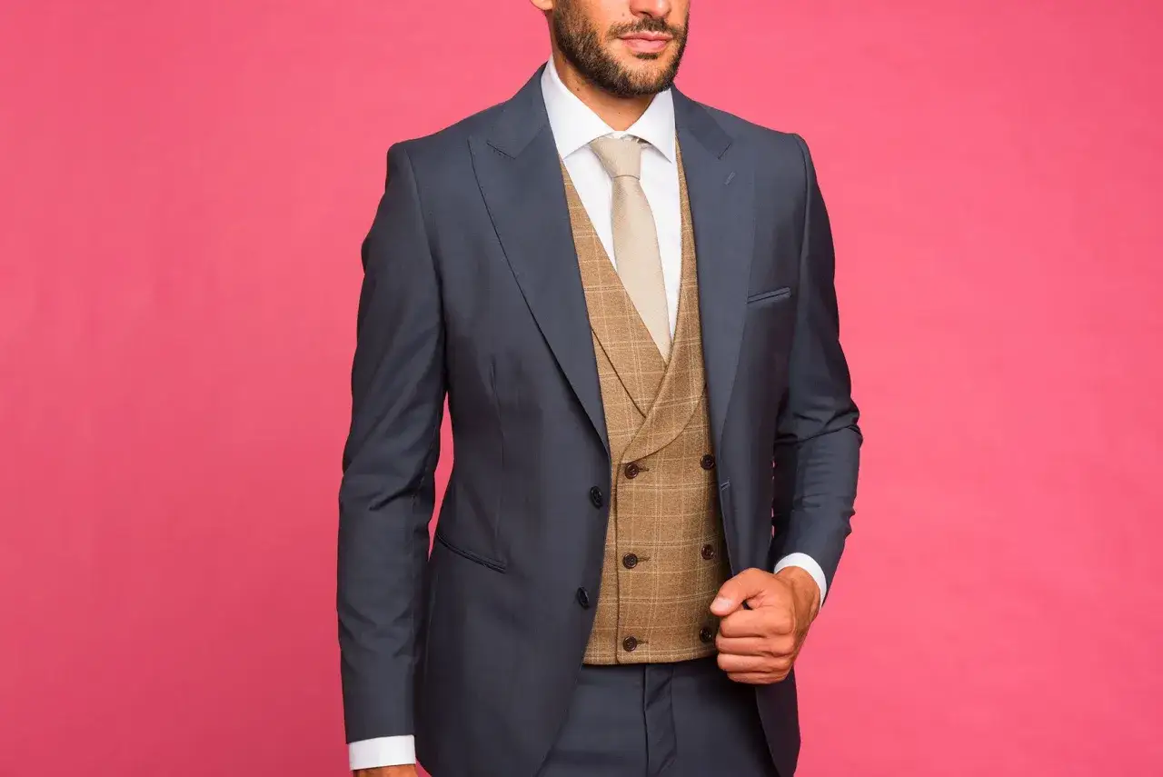 Uomo con completo blu scuro, camicia bianca, cravatta beige e un elegante gilet doppiopetto a quadri marrone.