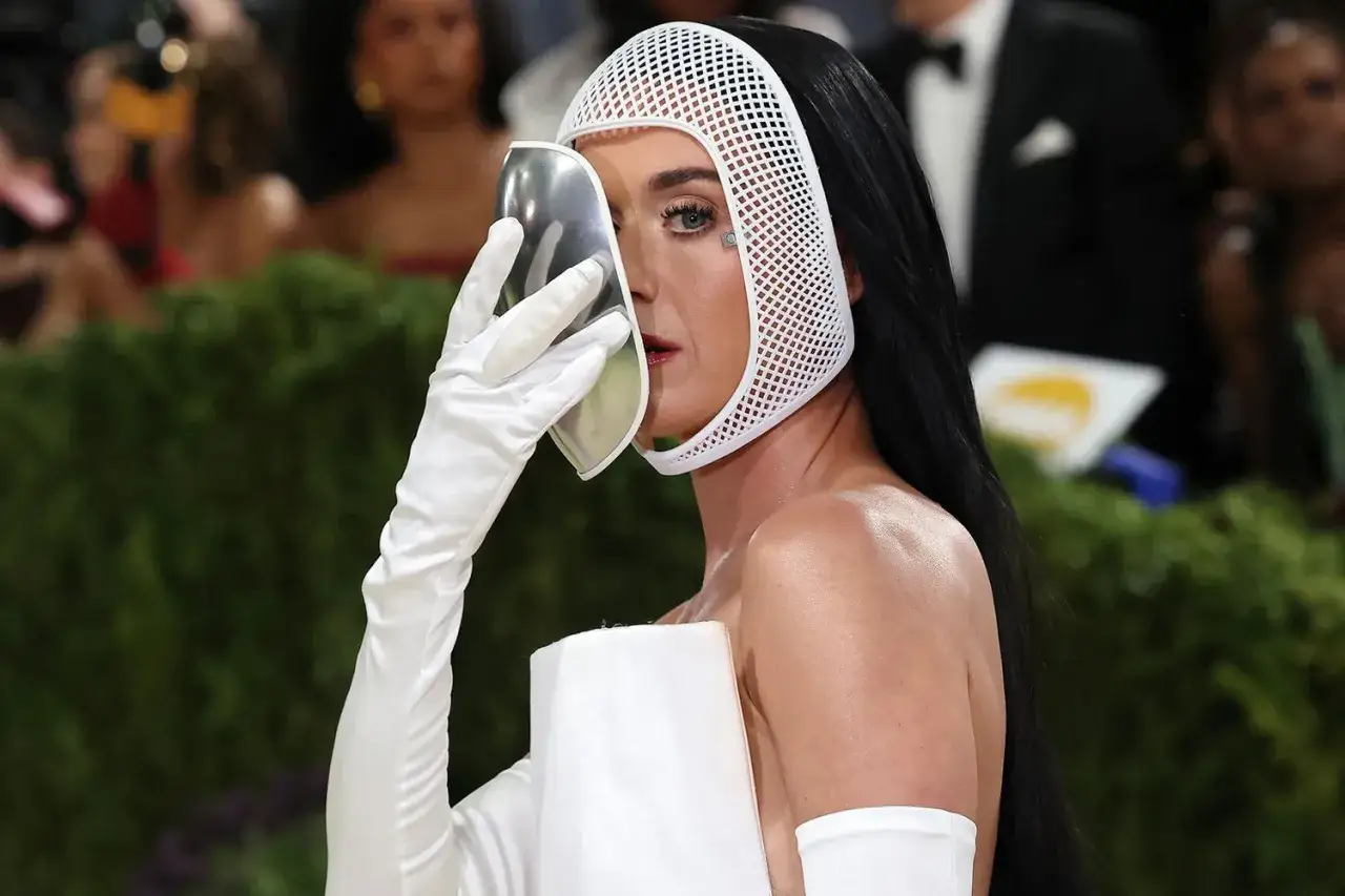 Katy Perry al Met Gala con un look futuristico, copre il viso con una maschera argentata e indossa un cappuccio bianco traforato.