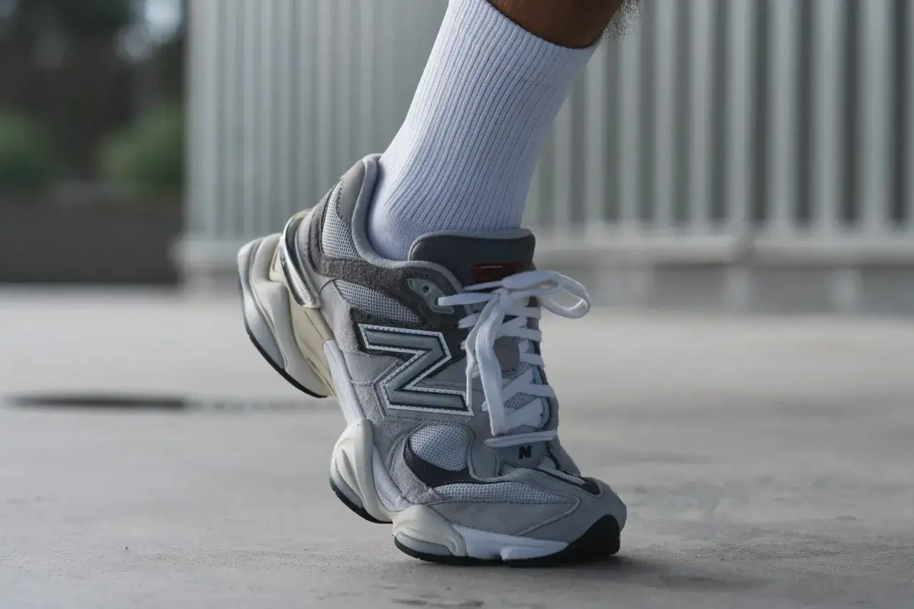 Il piede indossa una calza bianca e una New Balance 9060 grigia, mostrando come calzano queste sneakers.