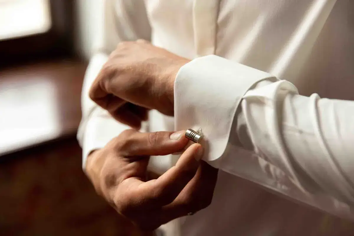 Uomo che allaccia gemelli a un polsino di camicia bianca. Diversi tipi di polsini camicia, come questo con gemelli, completano l'eleganza.