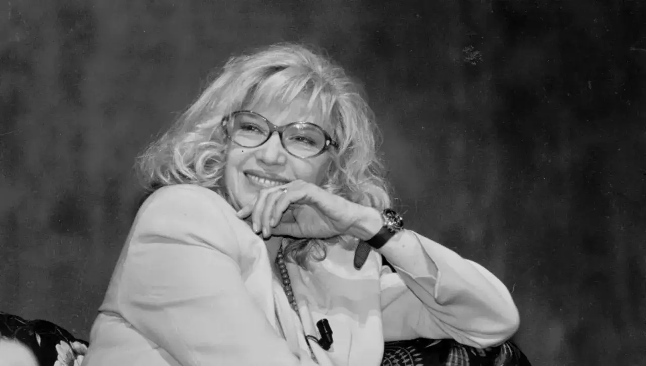 Monica Vitti, con i suoi capelli biondi e gli occhiali, sorride con un gesto elegante.